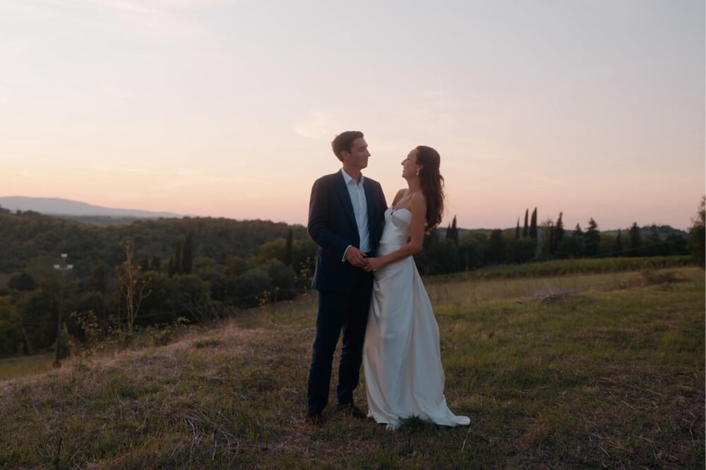 Couple standing together on a Tuscan hillside at sunset with cypress trees in the distance